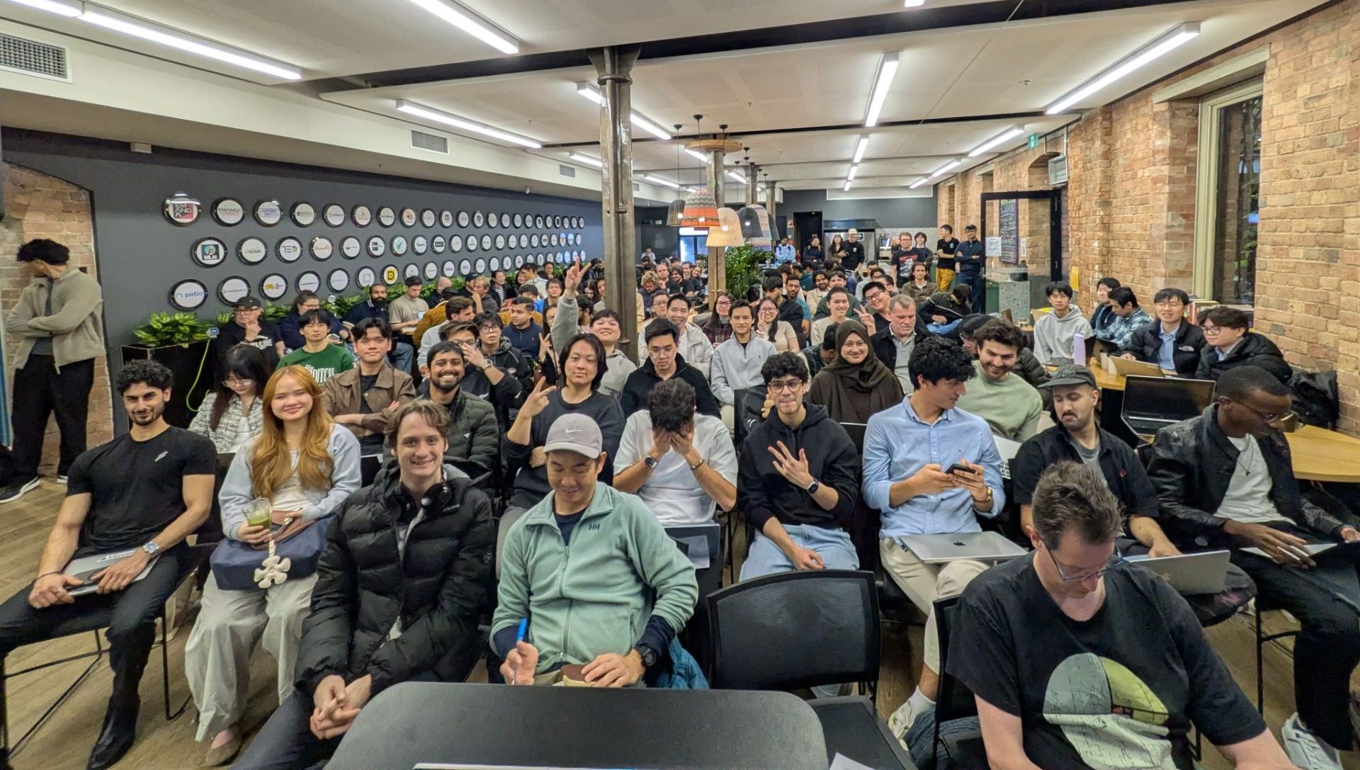 Wide view of the packed Watt the Hack audience seated at Stone & Chalk Melbourne under exposed brick and industrial lighting